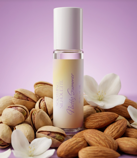 Nutty Summer 10 milliliter perfume oil bottle. Pistachios, almonds and jasmine as photo props on a light purple background. Original Price: $14. Comes in a roll-on glass bottle. Notes are pistachio, almond, salted caramel, jasmine, vanilla, sandalwood and heliotrope. Ingredients is Isopropyl Myristate and Fragrance
